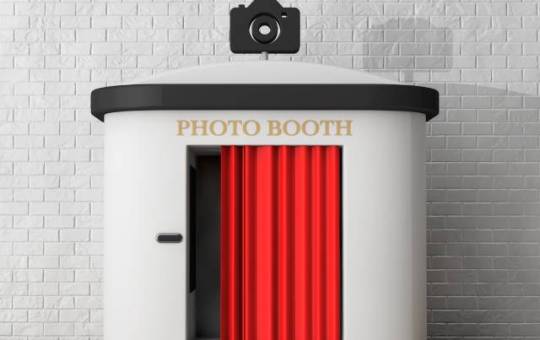 A 3D rendering of a white photo booth with a red curtain in a room with white-brick walls and a wooden floor.