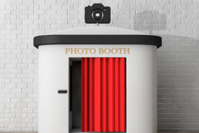 A 3D rendering of a white photo booth with a red curtain in a room with white-brick walls and a wooden floor.