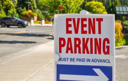A sign that reads "Event Parking, must be paid in advance" in red and blue letters sits at the entrance to a parking lot.