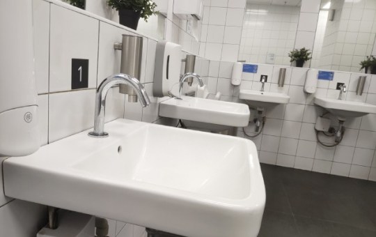 A modern commercial bathroom with a standard design upgraded to include touchless faucets and automatic soap dispensers.