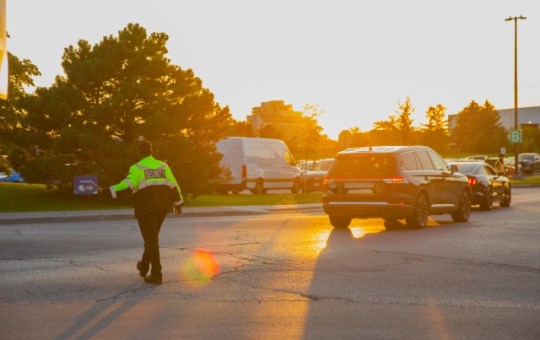 A security guard controlling event traffic. He holds his left hand out as he looks to the right at a full parking lot.