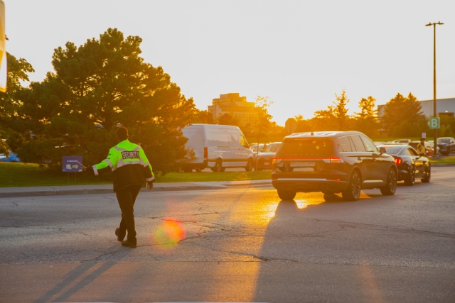 A security guard controlling event traffic. He holds his left hand out as he looks to the right at a full parking lot.