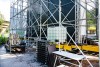A metal scaffolding structure that’s been set up outdoors for an event with tables and pallets sitting around it.