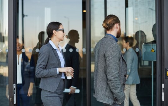 A group of professionally dressed business people walking in and out of an automatic revolving glass door.